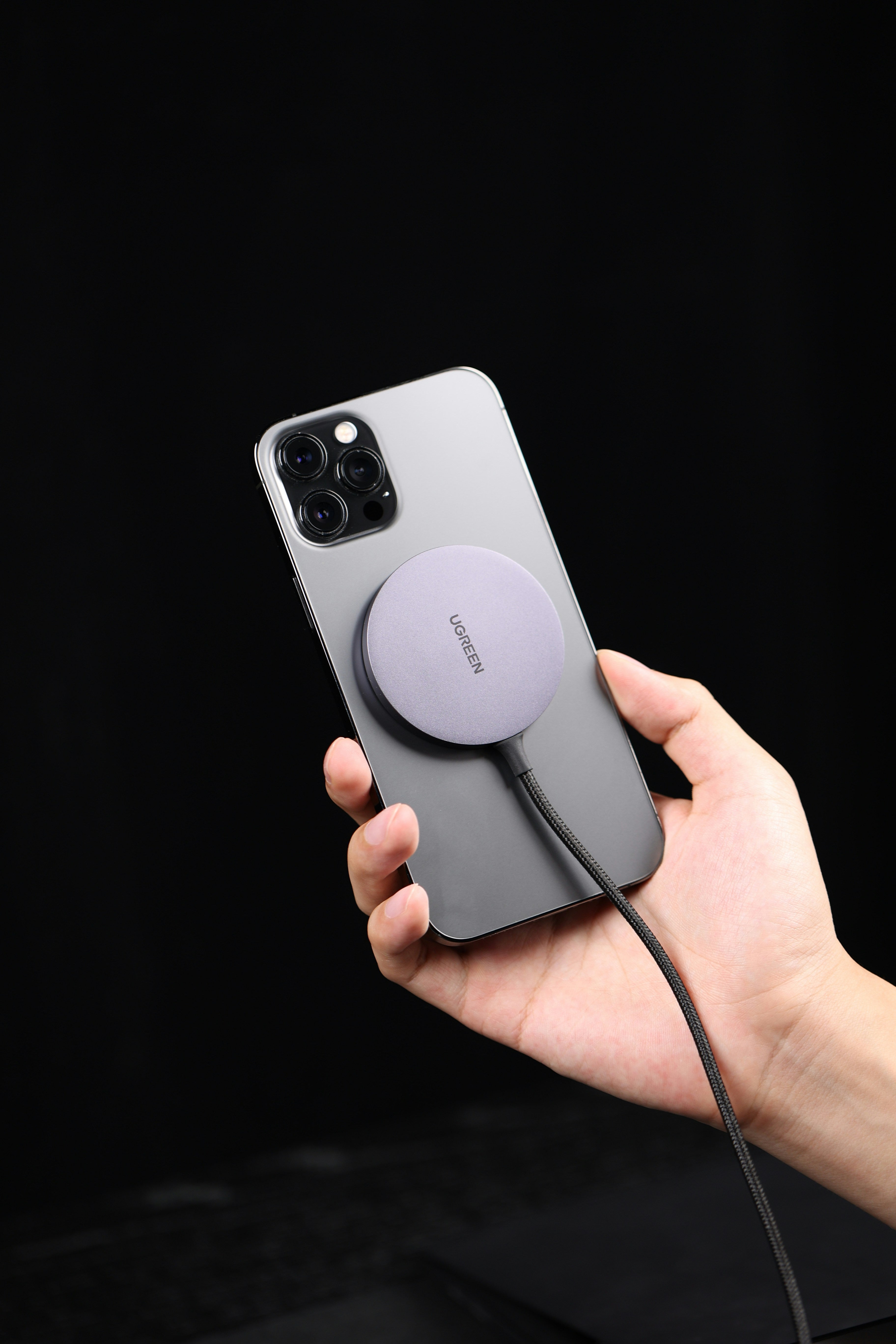 Hand holding a smartphone with a magnetic charging pad on a black background
